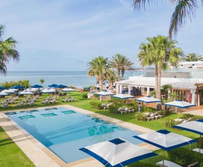 Zona exterior ajardinada con piscina y mobiliario de este hotel junto al mar.