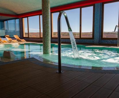Amplia piscina de hidroterapia con amplios ventanales y vistas del spa del hotel.